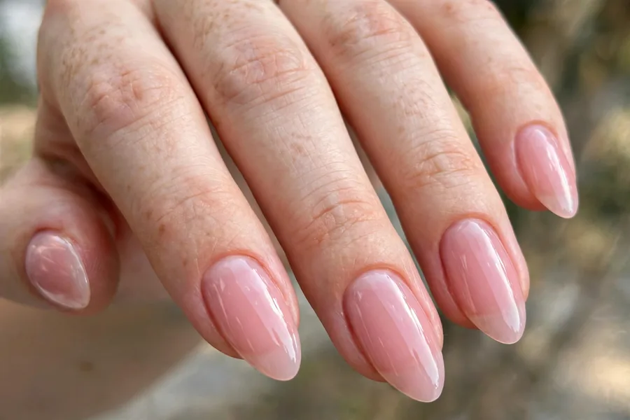 Real hand with sheer baby pink lip gloss nails, ultra glossy wet-look finish