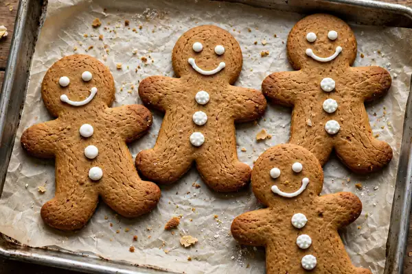 Gingerbread men cookies with white icing smiles and buttons on a baking sheet