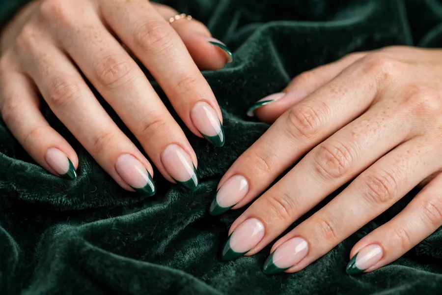 Emerald green Christmas French tip nails on real hands resting on dark green velvet