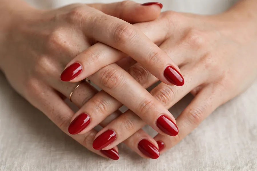 Classic true red almond nails on real hands with fingers gently interlaced