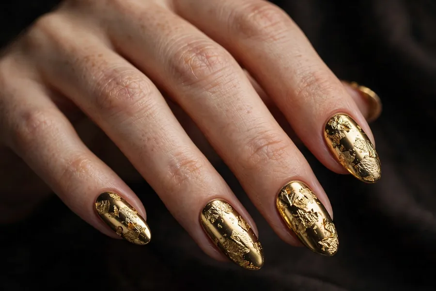 Hand with gold chrome nails covered in antique gold foil flakes