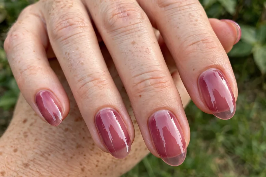 Real hand with sheer berry plum lip gloss nails, glassy juicy shine
