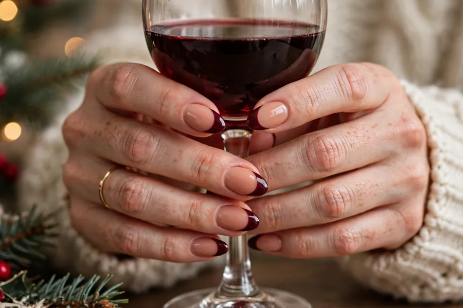 Burgundy wine Christmas French tip nails on real hands holding a glass of red wine