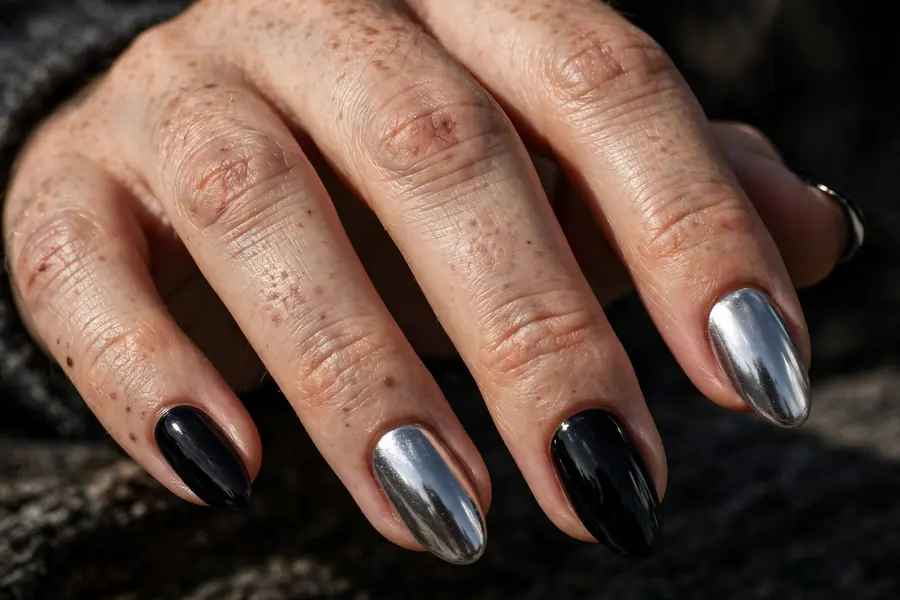 Silver chrome nails with black accent nails on real hands against a black background