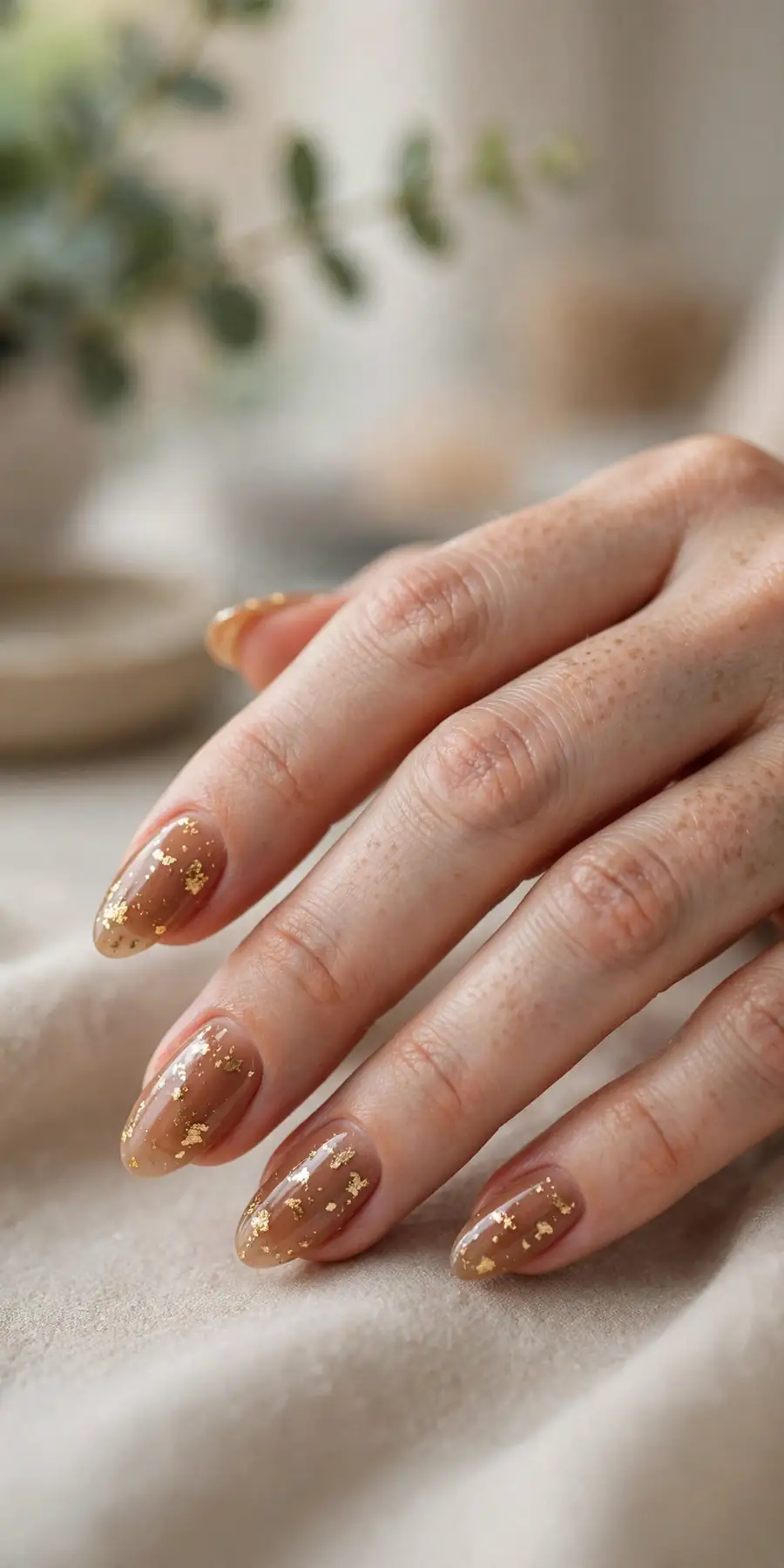 Caramel nude nails with delicate gold foil flakes on almond nails