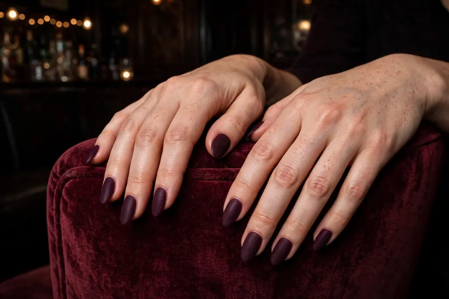 Deep plum velvet matte date night nails on real hands in a dim jazz lounge