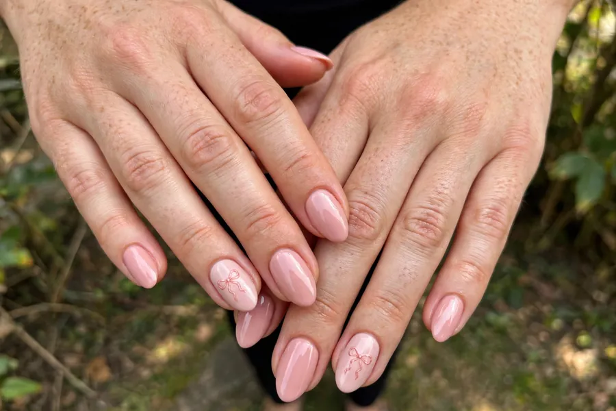 Blush nails with tiny bow accents on real hands