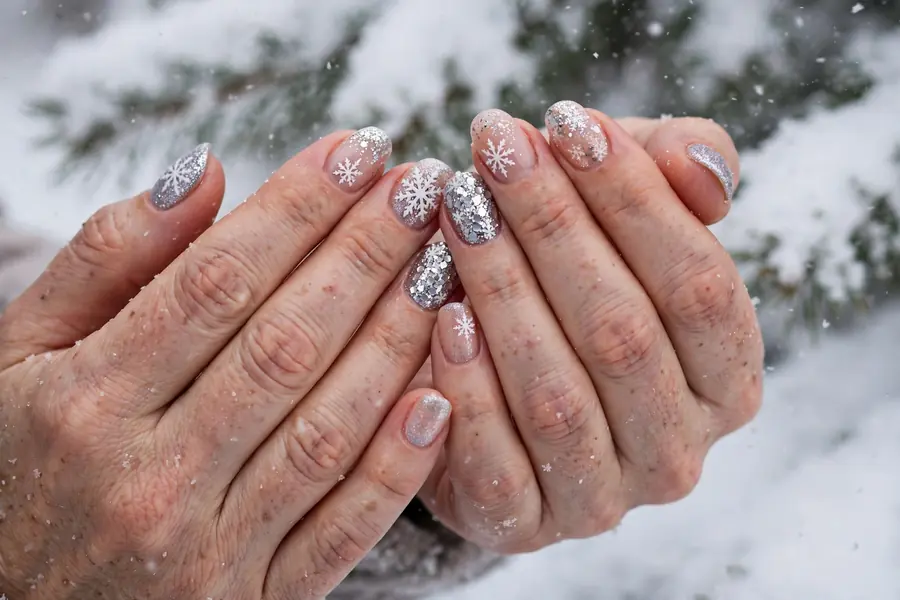 Snowflake glitter accent nails on real hands in snowy light