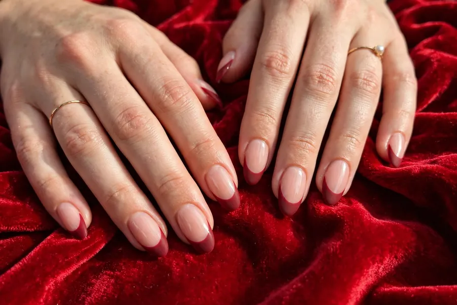 Velvet matte red Christmas French tip nails on real hands on red velvet fabric