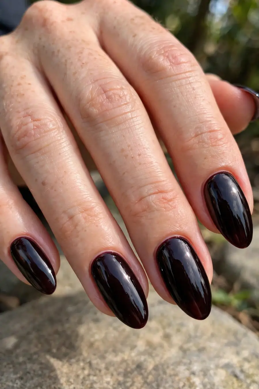 Real hand with deep black cherry lip gloss nails, vampy high-shine finish