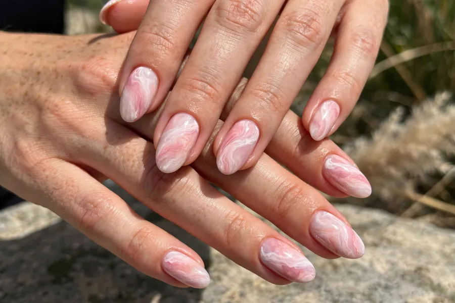 Blush marble nails on real hands with soft pink and white swirls