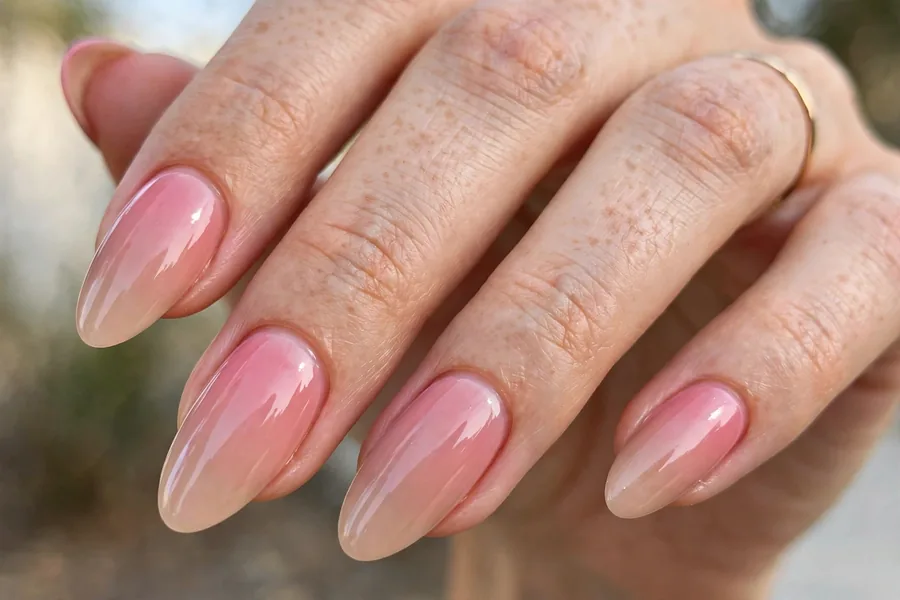 Real hand with pink to nude ombre lip gloss nails, glossy gradient finish