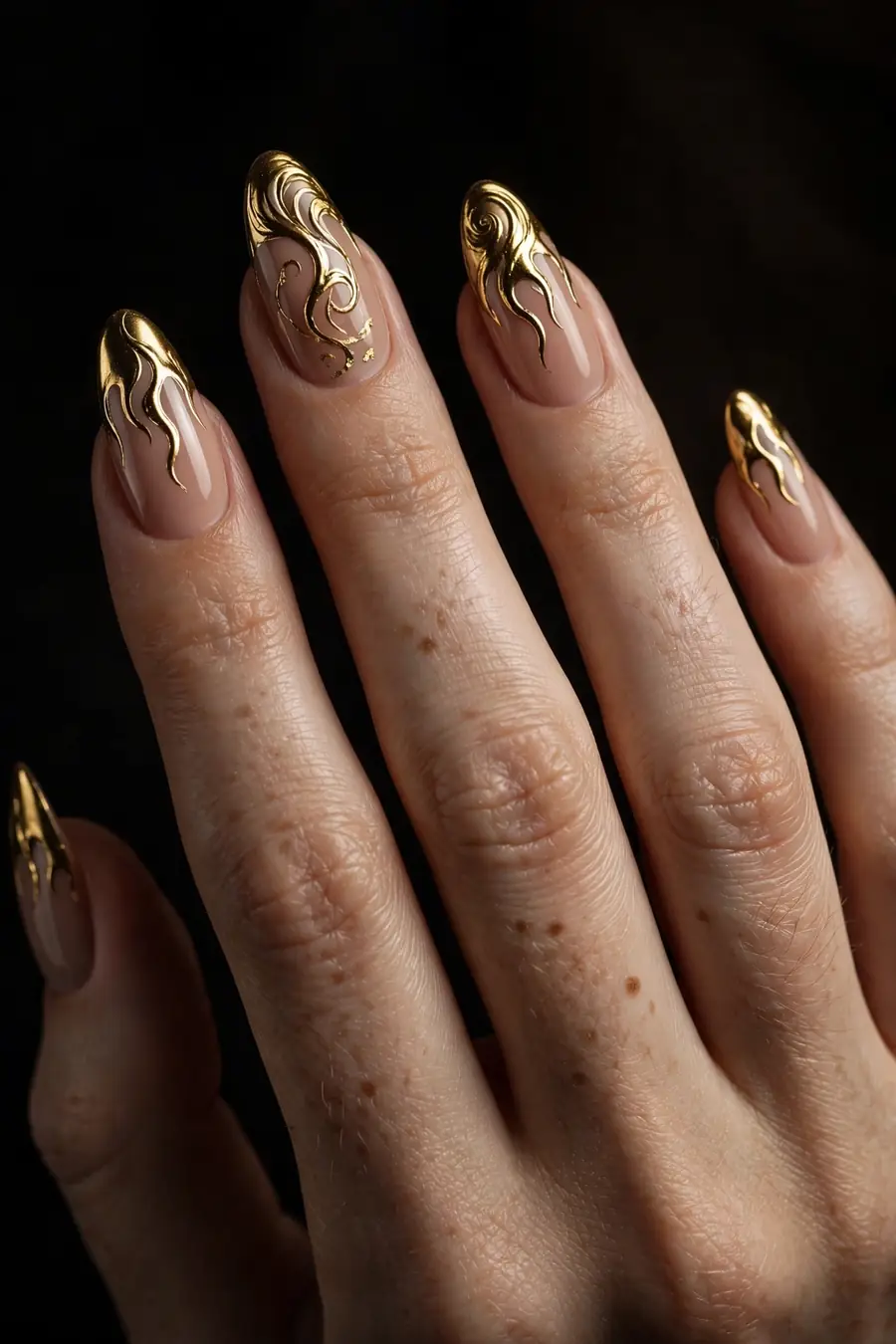 Hand with nude nails and hand-painted gold chrome flames