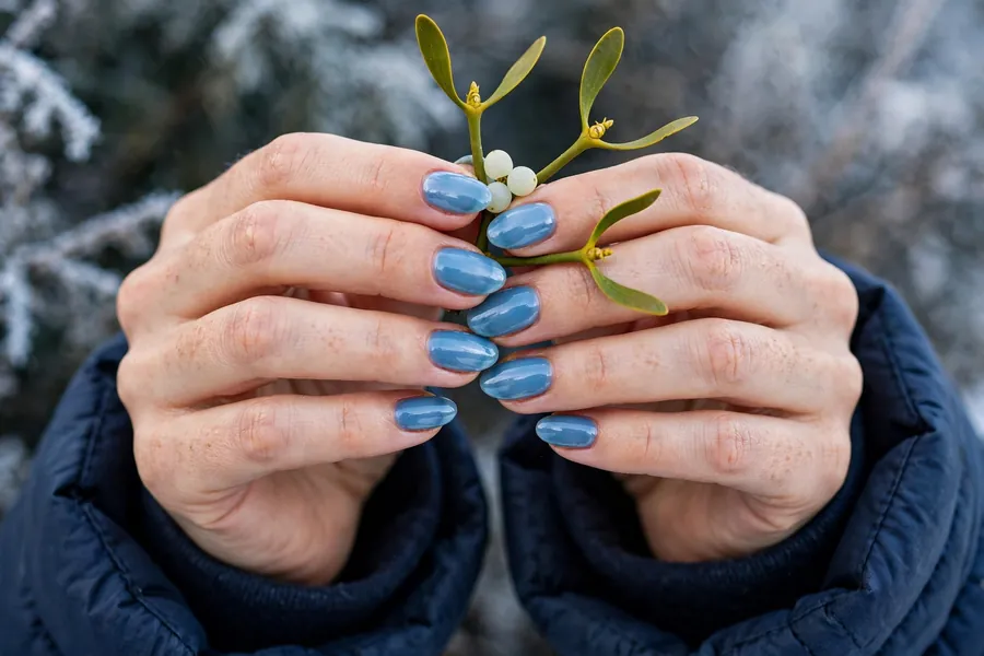 Mistletoe sprig on icy blue mistletoe nails on real hands with a winter coat