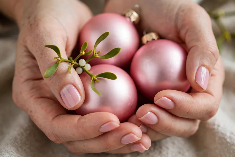 Mistletoe sprig on soft pink mistletoe nails on real hands holding pink ornaments