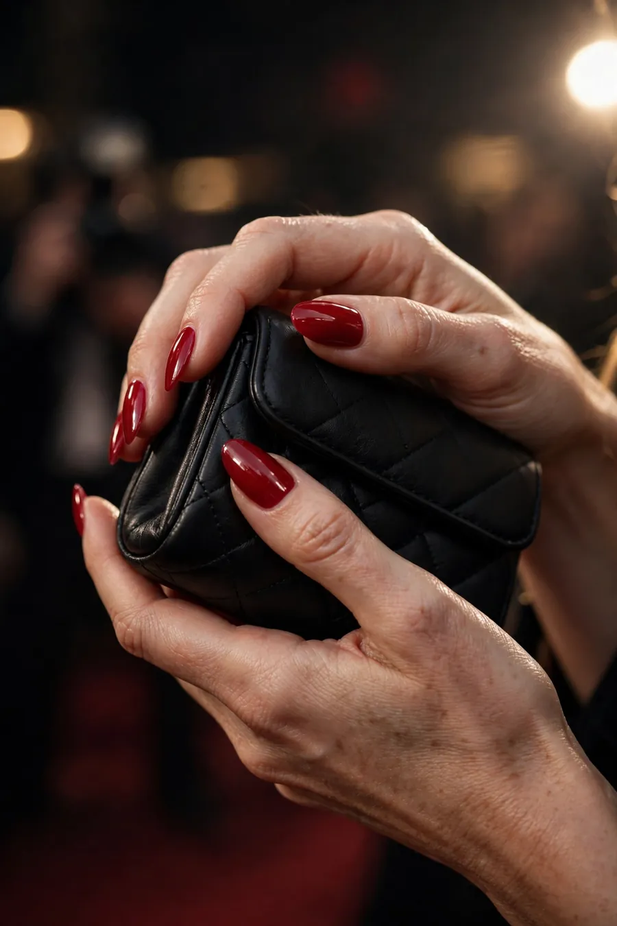 Classic red long almond nails on real hands holding a black evening clutch