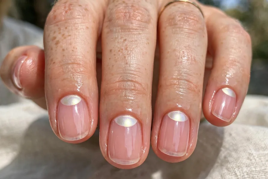 Real hand with glossy reverse French manicure, sheer pink with glowing half moons